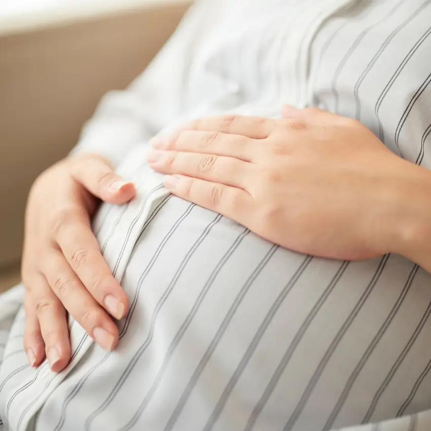 Close-up of a pregnant belly cradled by hands on a striped shirt silhouette, conveying expectant motherhood.